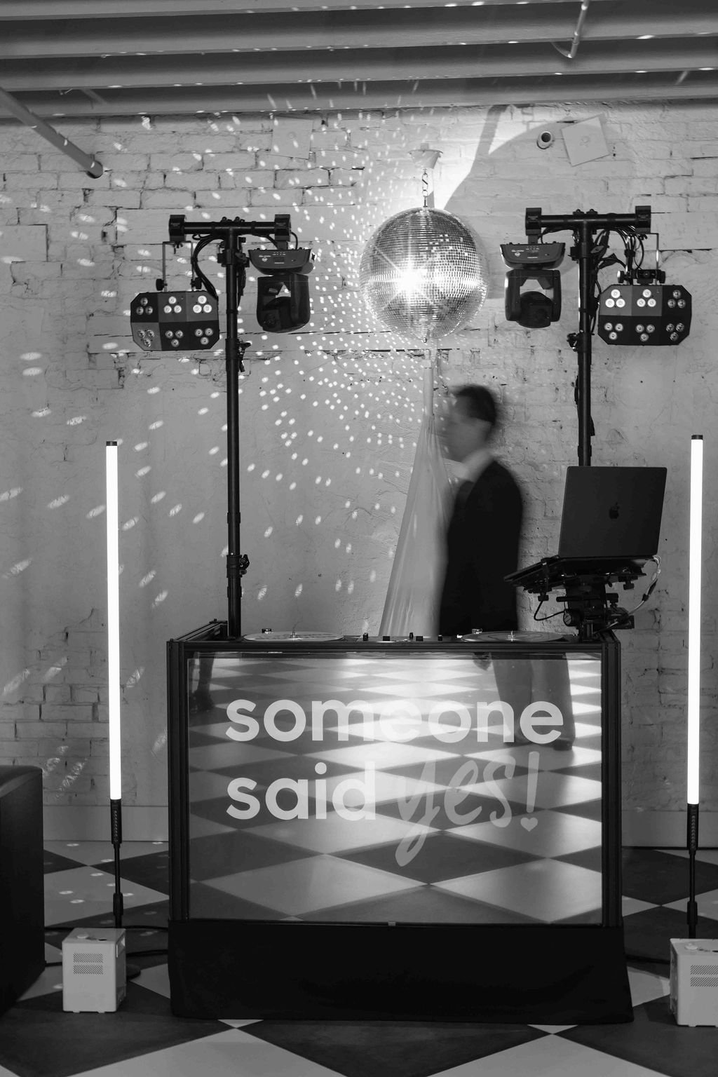 The DJ booth under a mirror ball and moving lights, the DJ a motion blur behind the decks