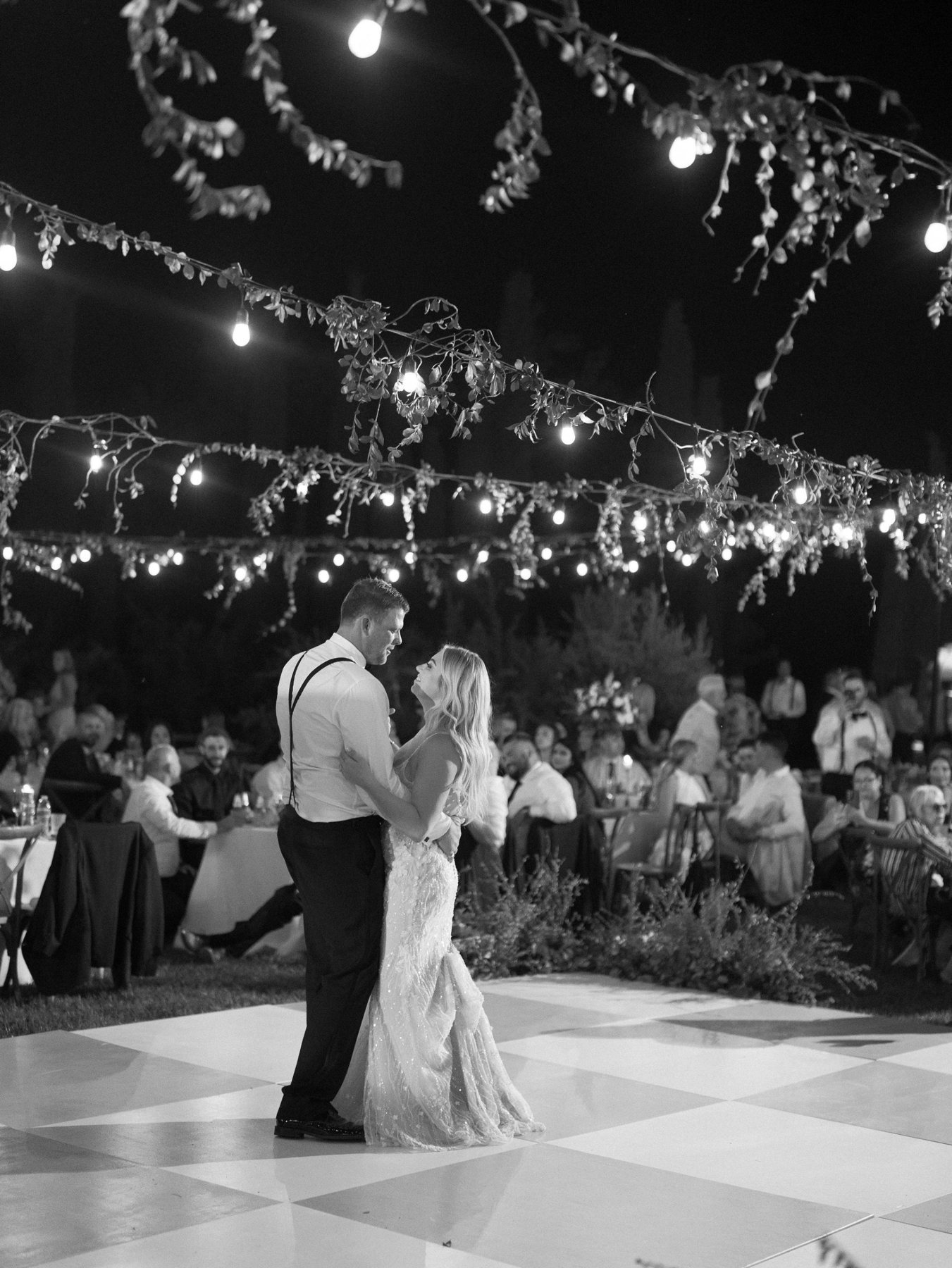 A couple sharing their first dance on a checkered floor under string lights