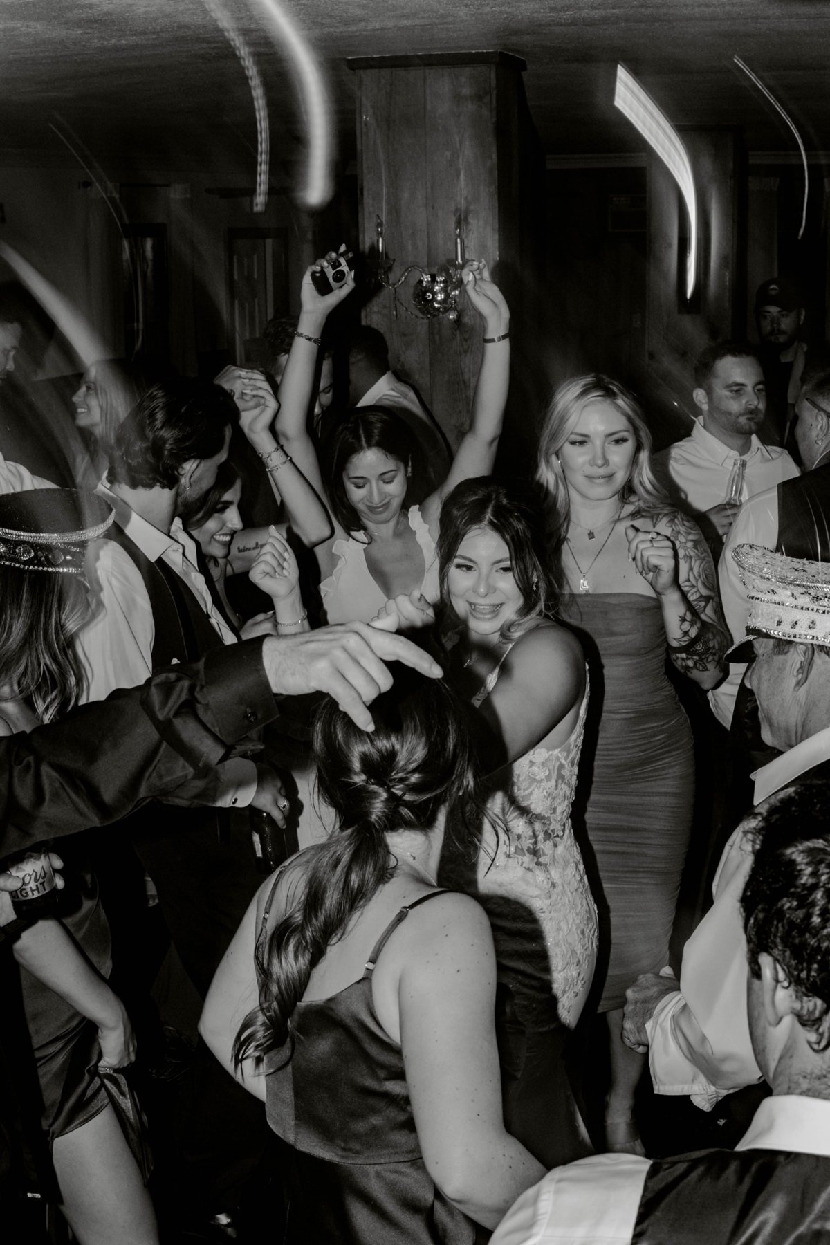 Wedding guests dancing with arms up around the bride under swirling party lights