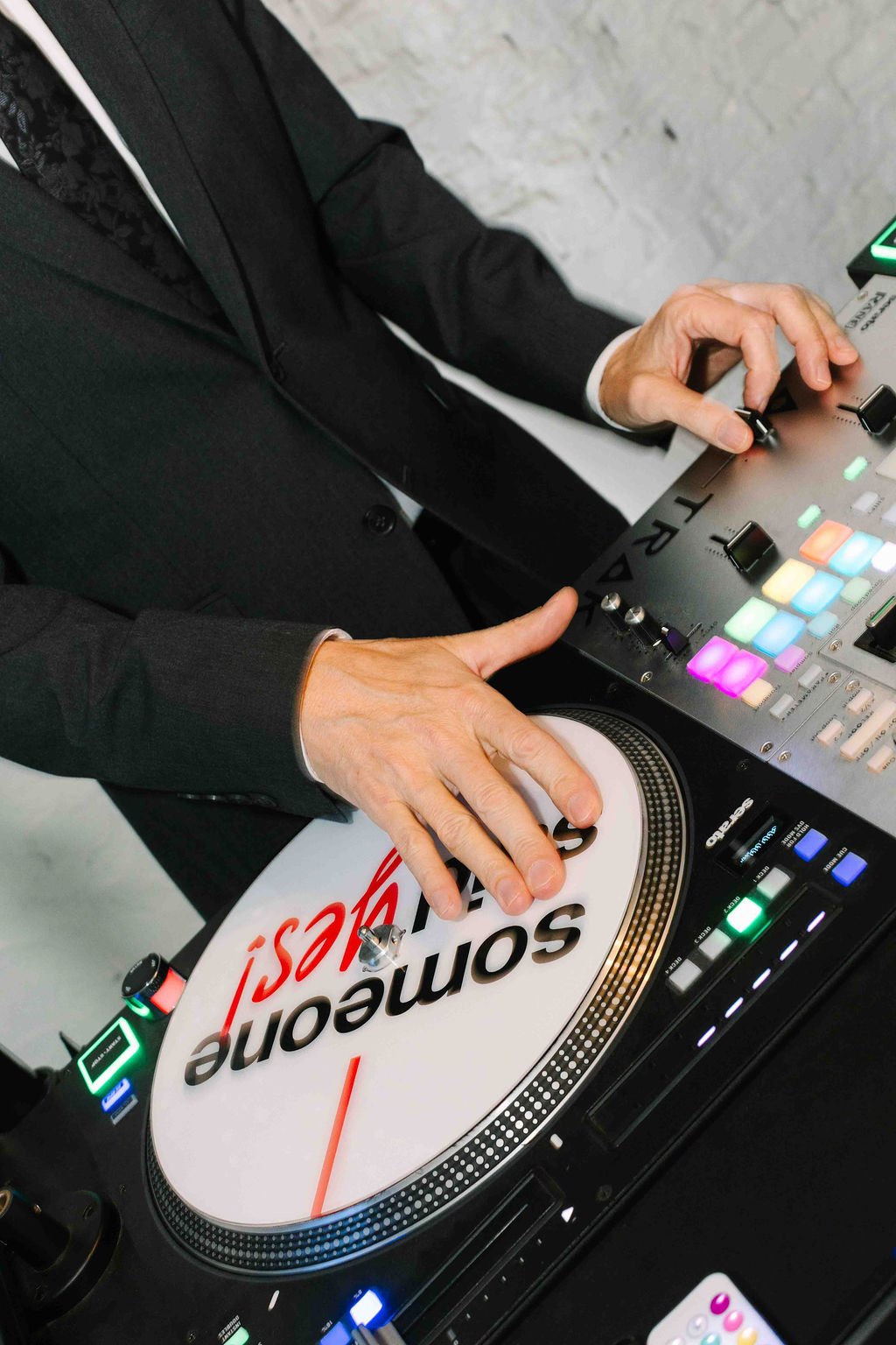 Hands on a turntable and mixer, mid mix, with glowing pads